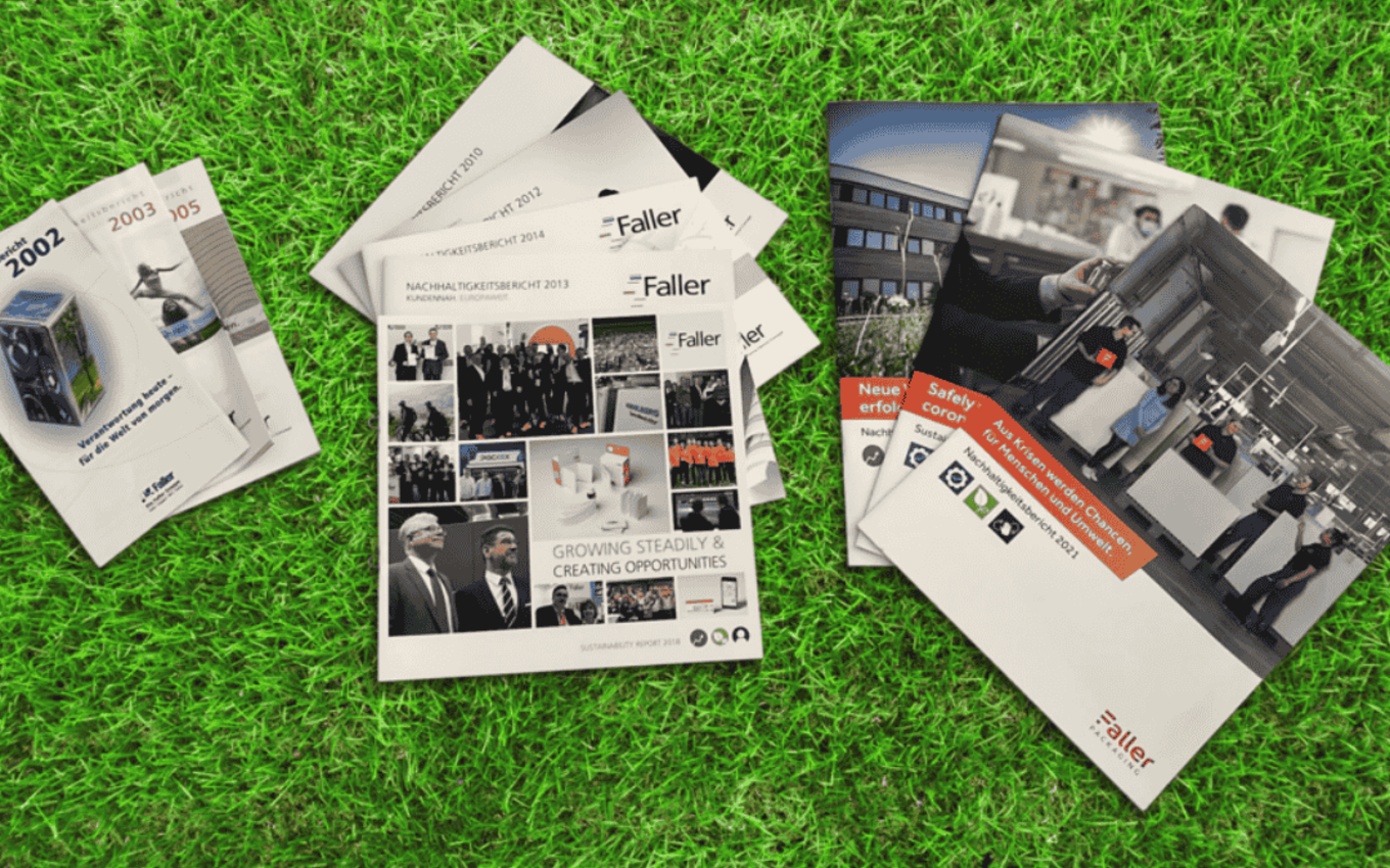 Mehrere Nachhaltigkeits- und Geschäftsberichte von Faller Packaging liegen auf einer grünen Wiese. Die Titel zeigen die Entwicklung des Unternehmens über die Jahre hinweg – von frühen Berichten bis zu aktuellen Ausgaben mit Fokus auf Nachhaltigkeit, Wachstum und Zusammenarbeit.